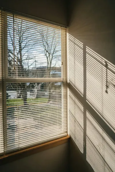 25mm aluminium venetian blinds in cream on a corner window with sunlight stripes on the wall