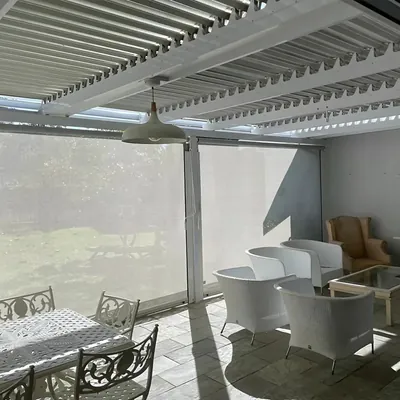 Light sheer outdoor screen blinds under a white louvred roof on a patio with lounge chairs