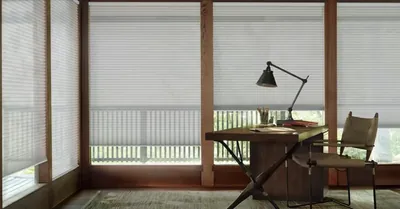 Pale honeycomb blinds on a glazed study with a timber desk and lamp