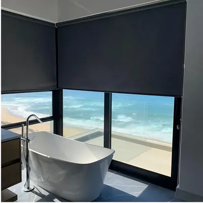 Charcoal blockout roller blinds in a bathroom with freestanding bath and ocean view