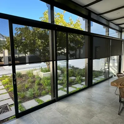 Charcoal sheer roller blinds beside aluminium sliding glass doors in a sunroom with garden view