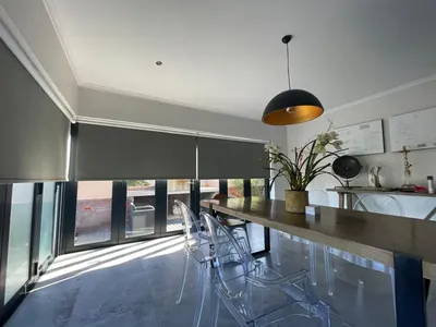 Dark grey blockout roller blinds over bifold glass doors in a dining room