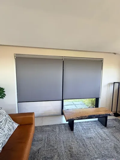 Two grey duo roller blinds with blockout lowered over sheer on living room doors