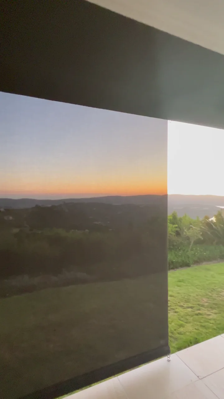 Charcoal outdoor screen blinds down across a patio at sunset, the view through the mesh still clear