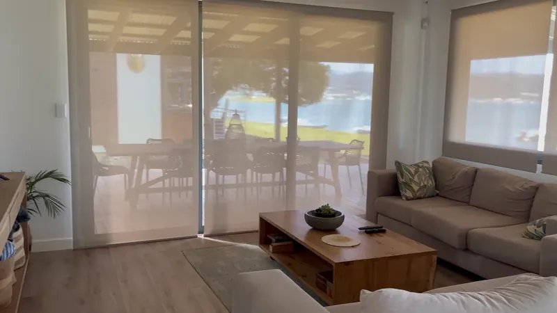 Sheer roller blinds across a living room window wall with a lagoon view beyond