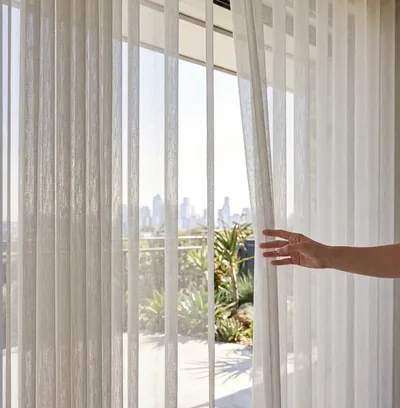 Sheer white vertical blinds at floor-to-ceiling glass doors, hand drawing one aside