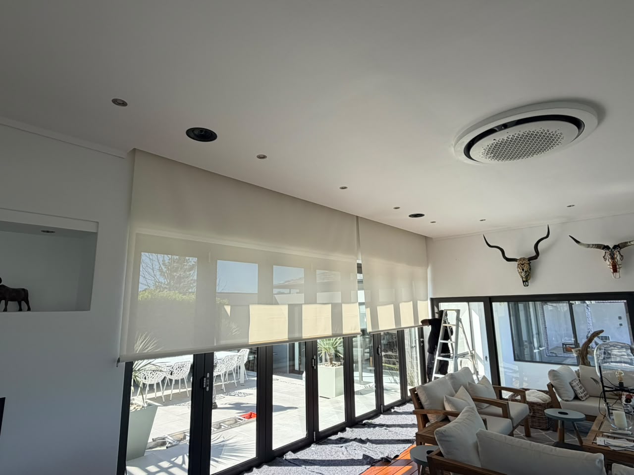 Custom Blinds Pearl White roller blinds covering glazed doors in a modern living room in South Africa