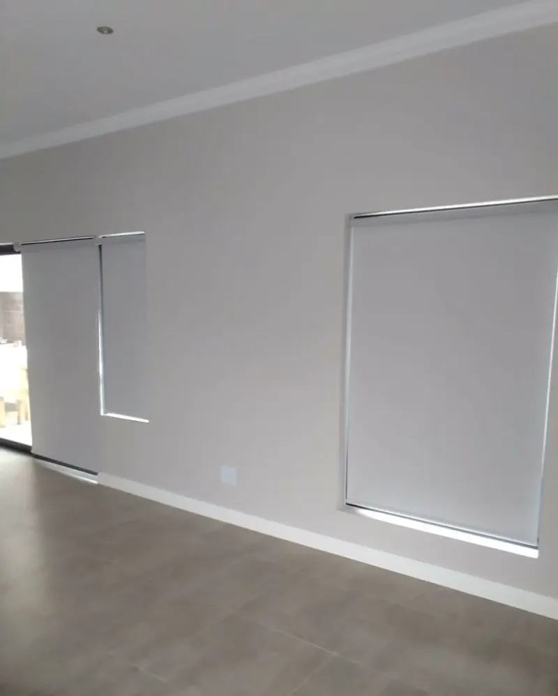 White blockout roller blinds on the windows and sliding door of an open tiled living room