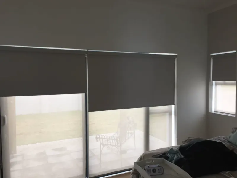 Charcoal duo roller blinds across bedroom patio doors, blockout half down over the sheer layer