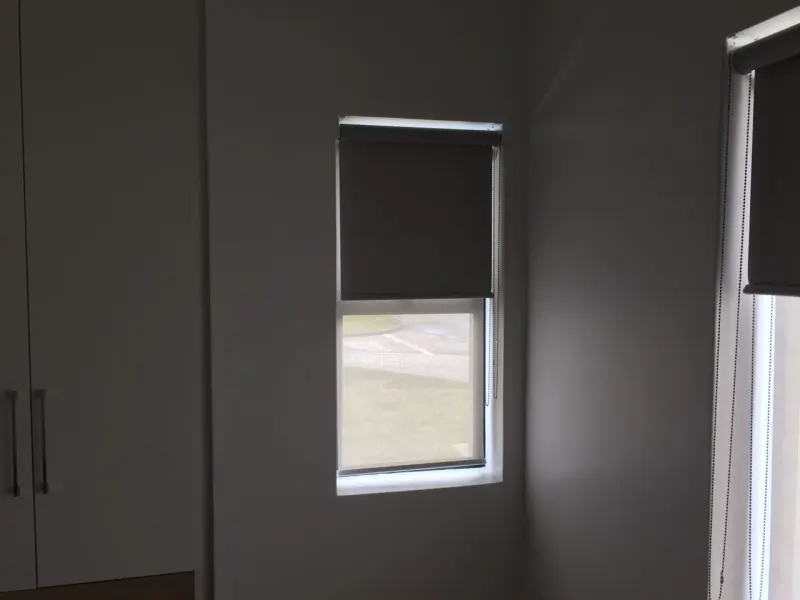 A charcoal duo roller blind part way down a small bedroom window, garden visible below the hem