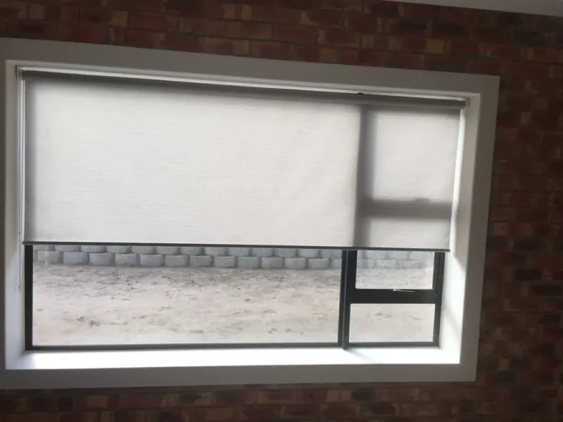 Cream roller blind part way down a window set in a face-brick wall, yard visible below