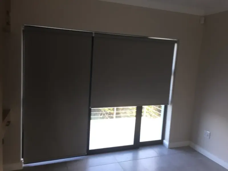 A taupe duo roller blind covering a wide sliding door onto a tiled patio