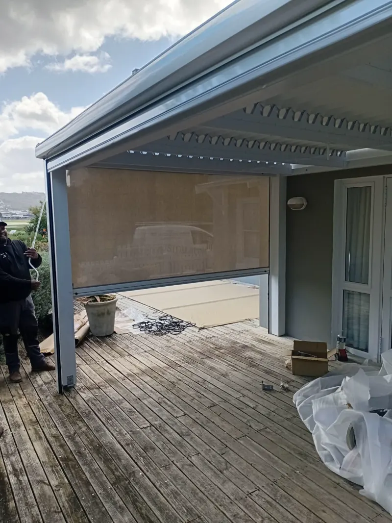 Outdoor screen blind on a timber deck under a pergola, the mesh clear enough to see straight through