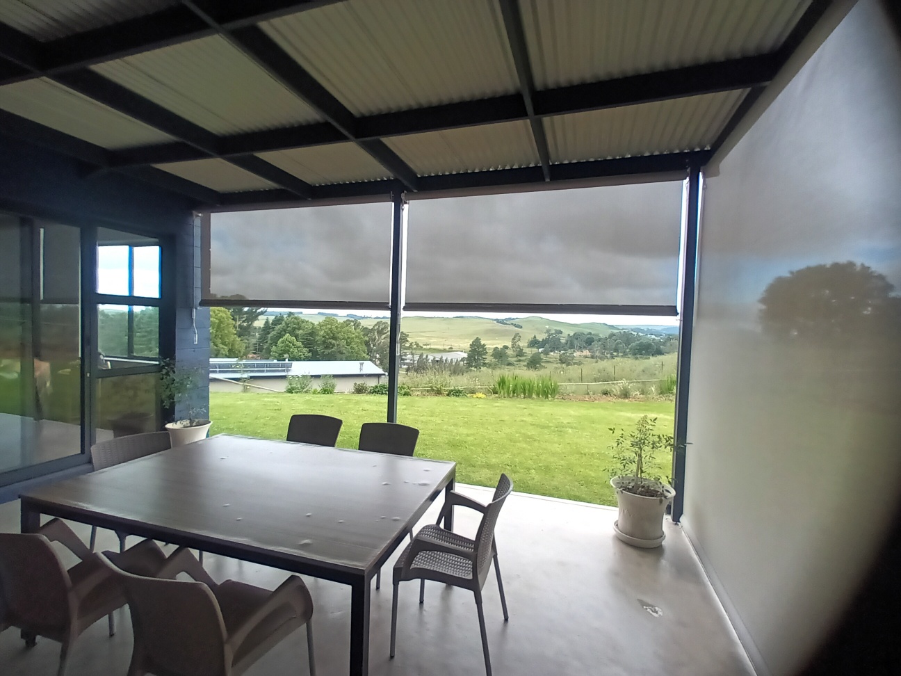Outdoor screen blinds in Almond sheerweave half-raised showing countryside and green hills beyond