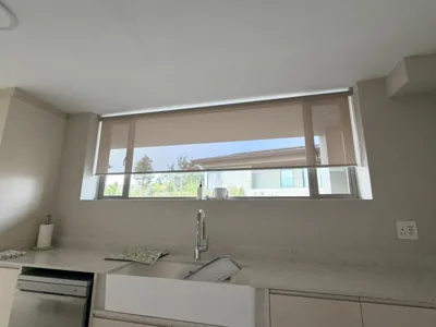 Beige sheer roller blind over a kitchen window above the sink
