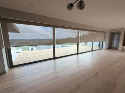 Beige sheer roller blinds across a glass wall in a wide living room