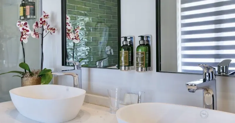 Zebra double roller blind reflected in the mirror above a green-tiled bathroom basin