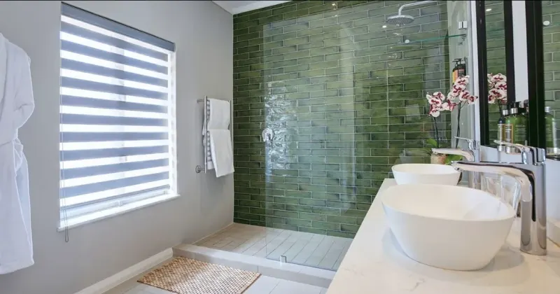 Wide view of a green-tiled bathroom, zebra double roller blind on the window beside the walk-in shower