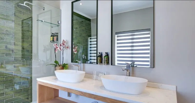 A zebra double roller blind half open over a green-tiled bathroom with twin stone basins
