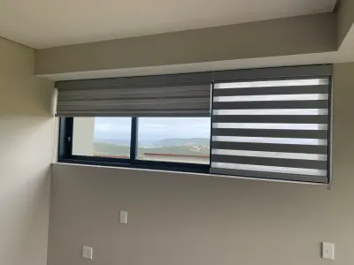 Grey zebra double roller blinds on a bedroom window with sea view
