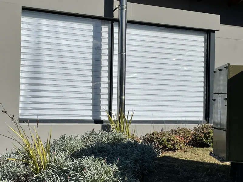 White zebra double roller blinds on two large windows, seen from the garden outside in full sun