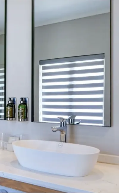Zebra double roller blind reflected in a bathroom mirror above a basin