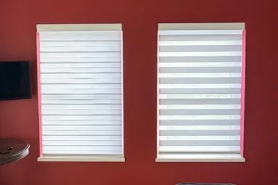 Two white zebra double roller blinds on windows against a red wall